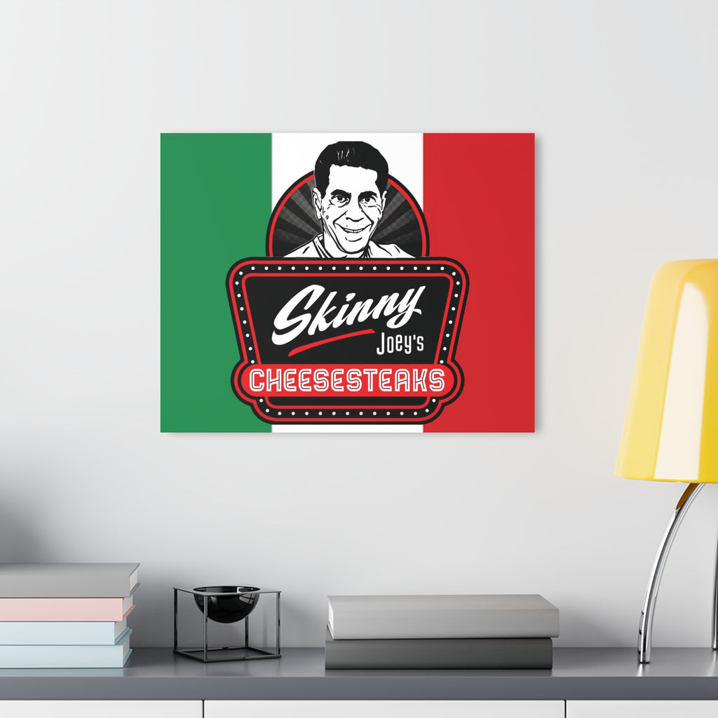 Poster of 'Skinny Joey's Cheesesteaks' on a wall above a desk with books and a lamp.