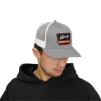 Man wearing a gray and white trucker hat with a logo on a white background