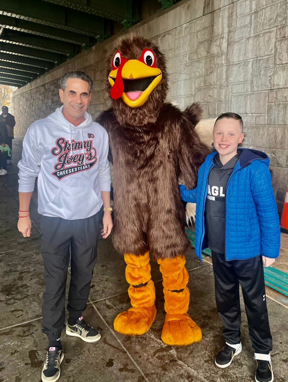 Two people posing with a person in a turkey mascot costume outdoors.